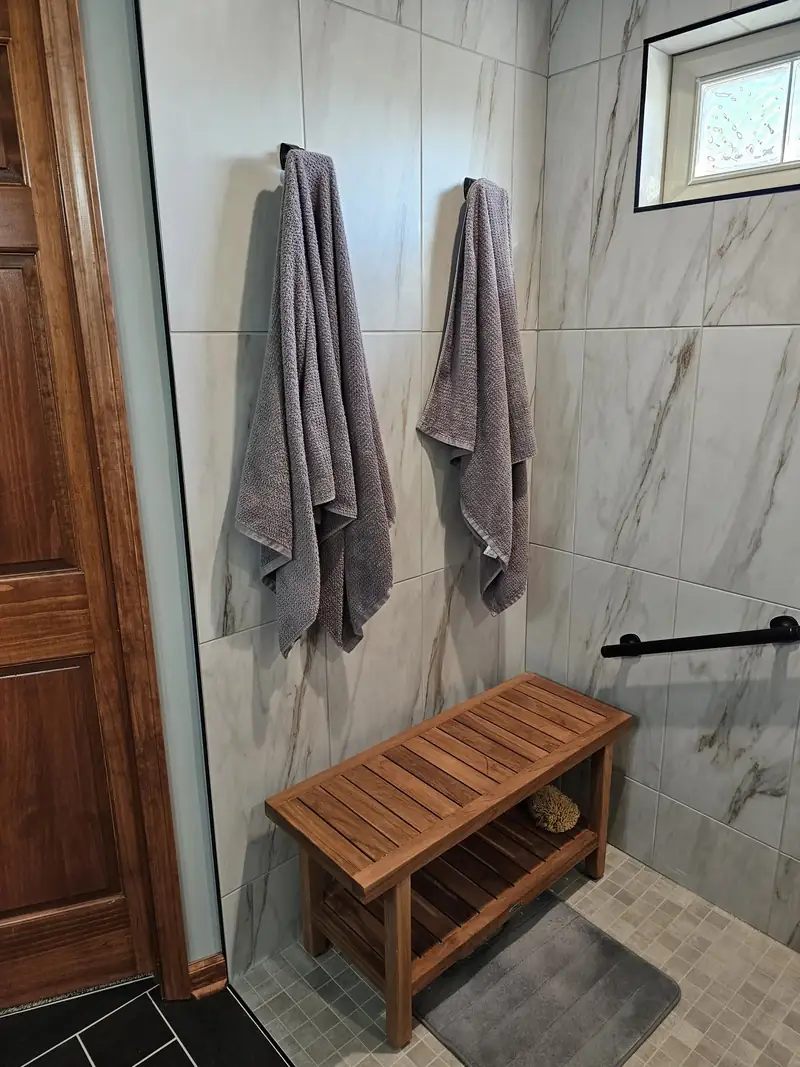 Curbless marble shower with a teak bench and horizontal grab bar