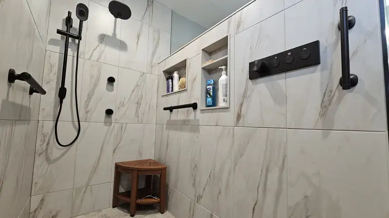 Marble-tiled walk-in shower with a teak bench and black fixtures
