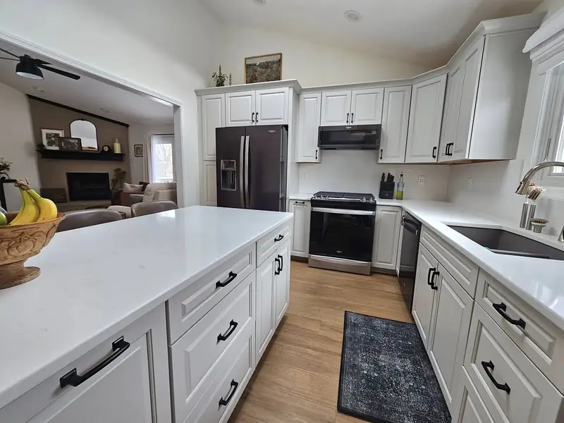 Remodeled subdivision kitchen with white cabinetry and quartz counters opening to a living room