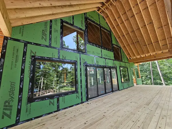 House sheathed and taped with large window openings facing the woods