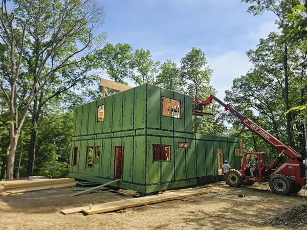 Telehandler lifting a framed wall panel into place on a wooded site